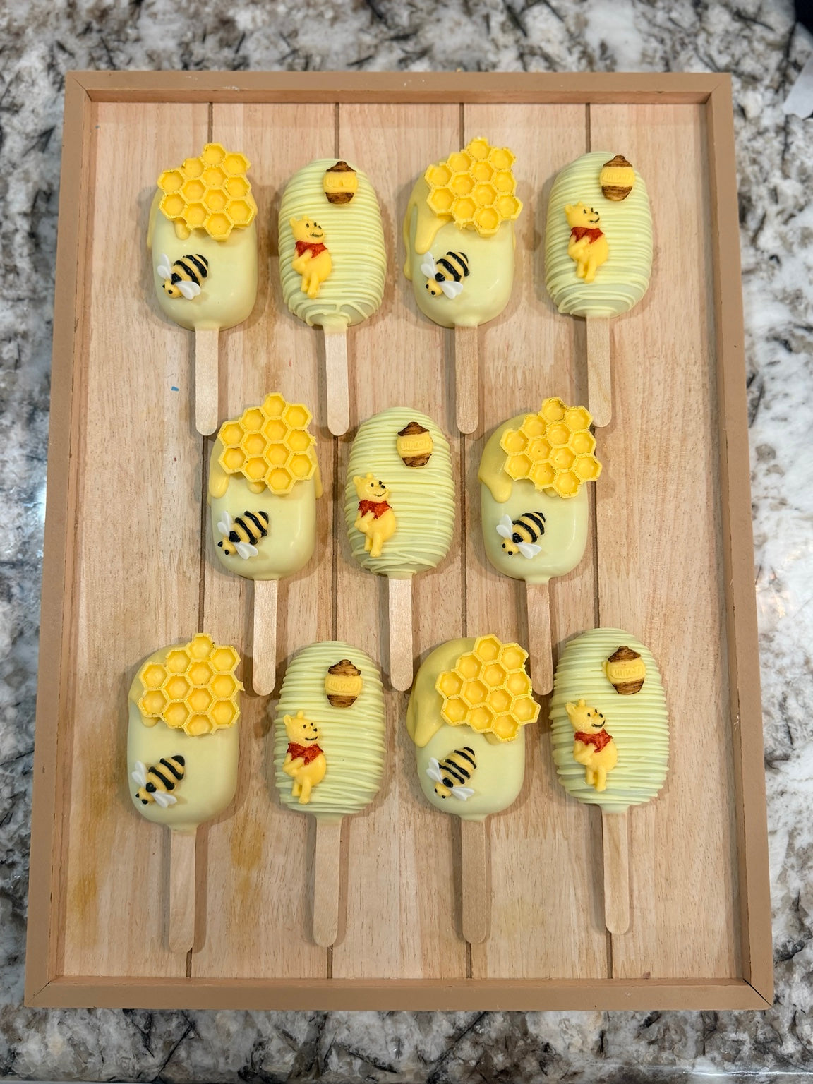 Handcrafted honey bear and bumblebee cakesicles displayed on a wooden tray
