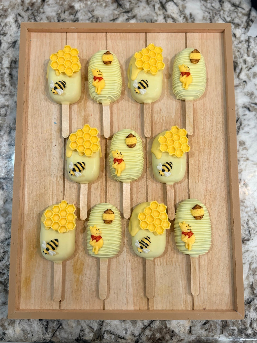 Handcrafted honey bear and bumblebee cakesicles displayed on a wooden tray